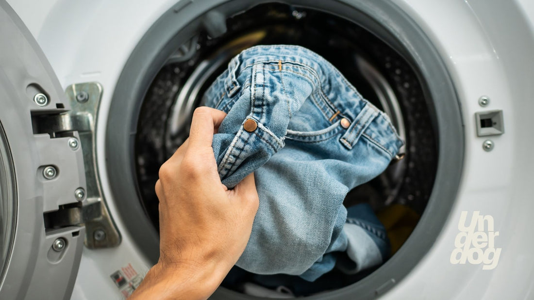 Une personne dépose un jean dans un lave-linge.