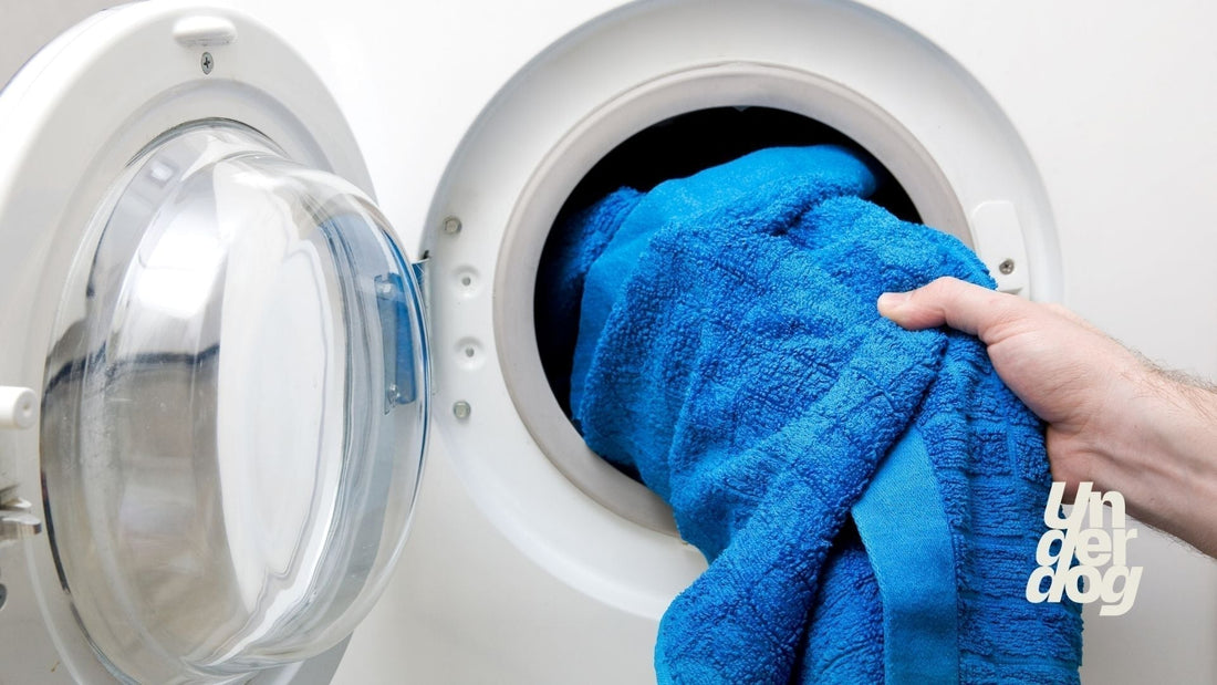 Une personne dépose une serviette de toilette dans un lave-linge.