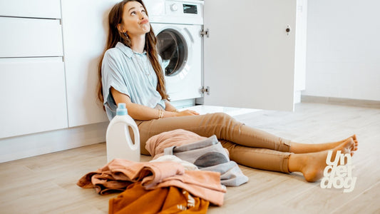 Une femme assise devant son lave-linge réfléchit en regardant le plafond.