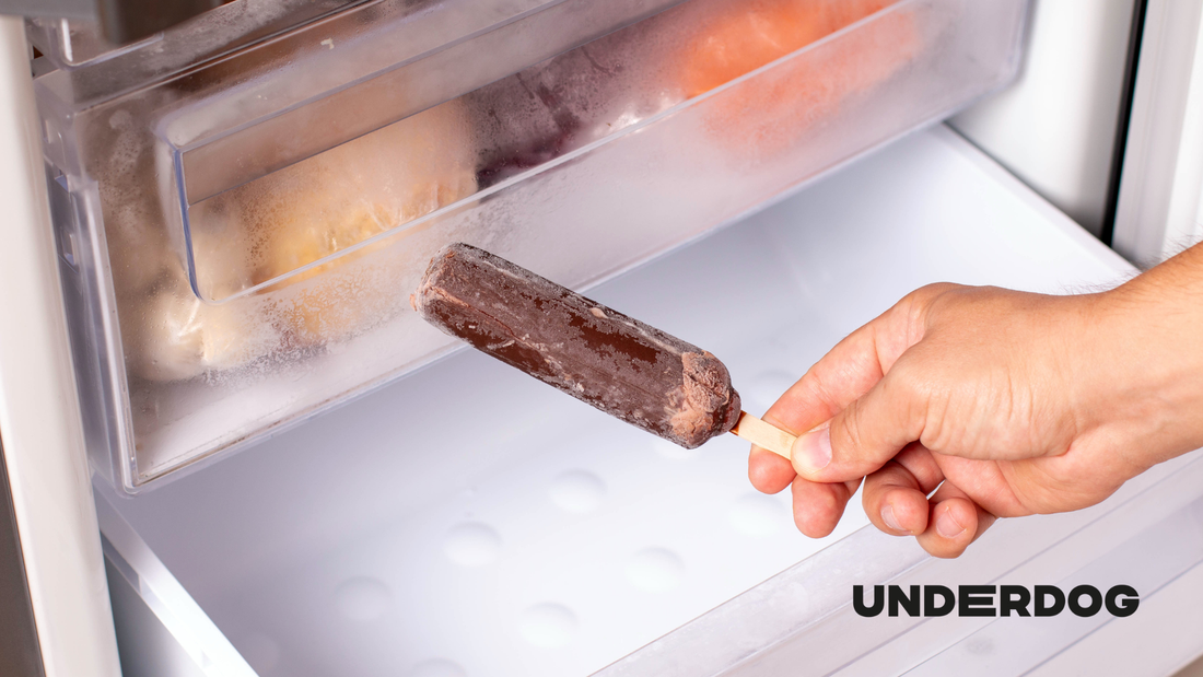 Une main tient un glace devant un congélateur