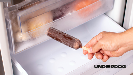 Une main tient un glace devant un congélateur