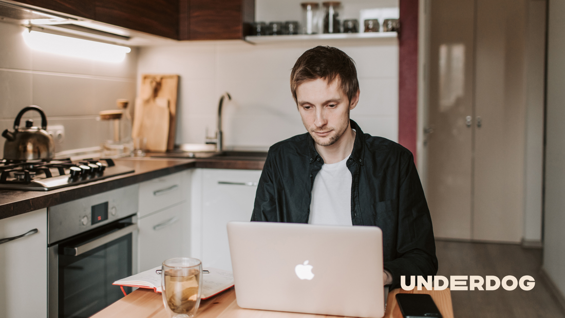Un homme travaille dans la cuisine sur son ordinateur portable tout en utilisant son téléphone