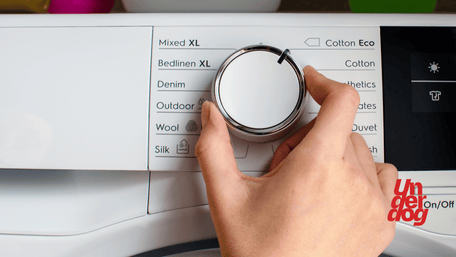 Une main règle la molette d'une machine à laver.