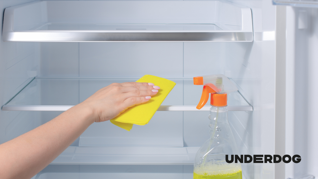 Une personne nettoie son réfrigérateur avec un pulvérisateur et un chiffon