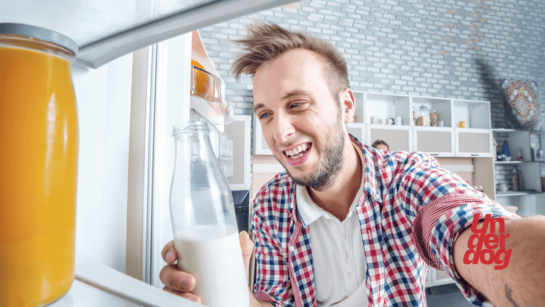 Un homme sourit avec du lait à la main en ouvrant son frigo.
