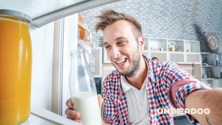Un homme sourit avec du lait à la main en ouvrant son frigo