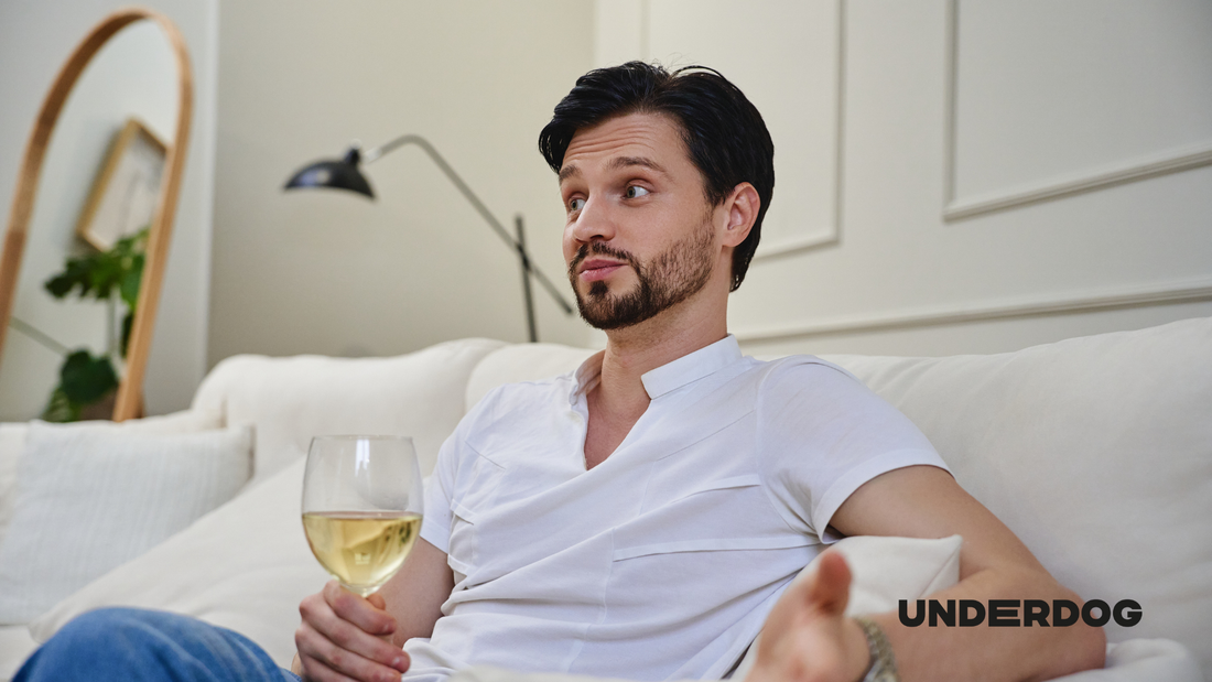 Un homme assis sur un canapé blanc tenant un verre de vin blanc