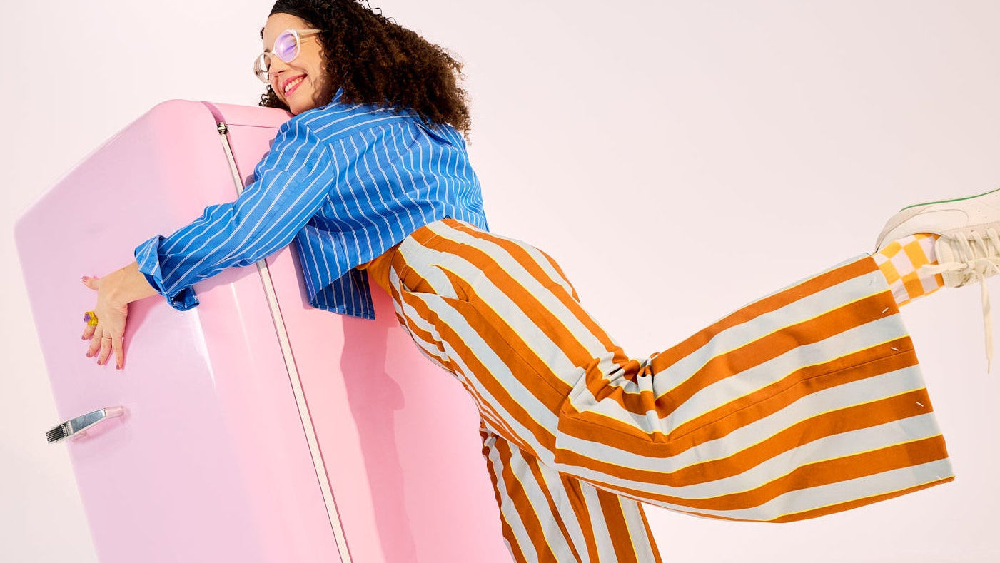 femme en habits rayés tenant un frigo rose dans les bras